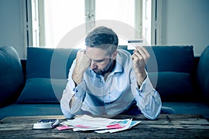 Upset man in stress paying credit card debts and counting finance with calculator and bank papers