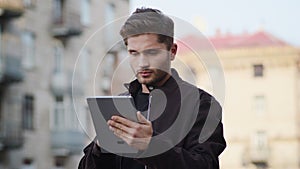 Upset man using tablet outside. Serious guy looking screen outdoors