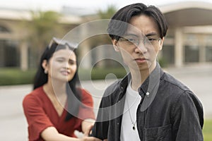 An upset or manipulative boyfriend, looking at the camera, leaving his remorseful and desperate girlfriend