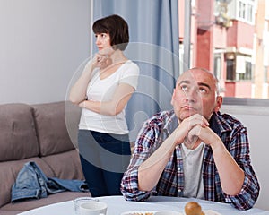 Upset mature man sitting while quarrel with wife at home interior