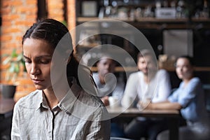 Upset mixed race woman suffering from bullying, sitting alone in cafe