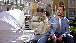 Upset mom worrying about crying baby pram, indifferent husband sitting on bench
