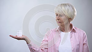 Upset old lady holding pills bottle, ineffective treatment, bad quality medicine