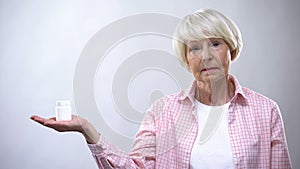 Upset old lady holding pills bottle, ineffective treatment, bad quality medicine