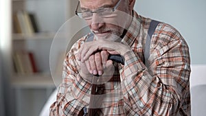 Upset old man leaning on walking stick, feels lonely, remembering youth, closeup