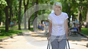 Upset old woman moving outdoors with walking frame, rehabilitation after trauma