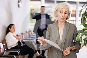 Upset old woman standing in waiting room with her back to person who is shouting at her