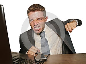 Upset and overwhelmed businessman in suit and tie working at office desk punching laptop computer suffering stress in financial