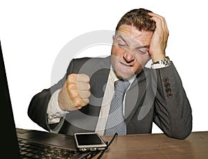 Upset and overwhelmed businessman in suit and tie working at office laptop computer desk punching mobile phone suffering stress in