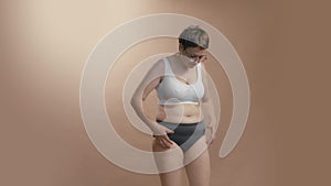 Upset plus size woman watching herself squeezing her abdomen fat. High quality medium full shot studio video.