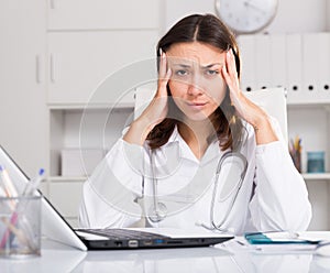 Upset practicioner girl is working with documents and laptop