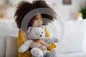 Upset preteen african american girl embracing teddy bear