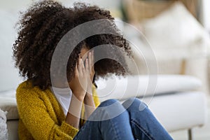 Upset preteen black girl sitting on floor at home, crying