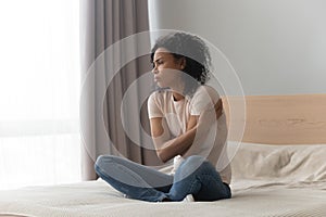 Upset sad African American woman sitting in bed alone