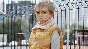 Upset, sad and lonely boy leaning on metal fence at public playground. Child depression, problems with bullying, victim in school