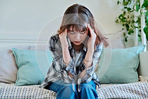 Upset sad young female sitting on couch at home