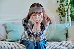 Upset sad young female sitting on couch at home
