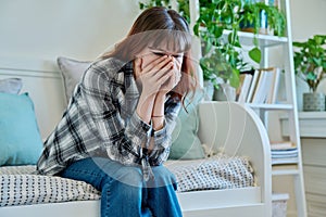 Upset sad young female sitting on couch at home