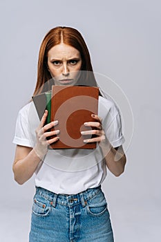 Upset sad young woman college student holding book and looking at camera on isolated background.