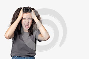 Upset screaming teenager girl suffering from loneliness, holding her head with her hands on a light background