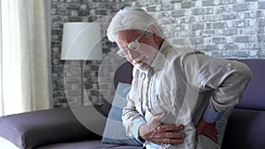 Upset senior elder man feel sudden back pain muscles ache tension injury sitting at home, sad old grandfather touching spine