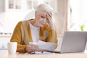 Upset senior lady reading bills, having financial troubles