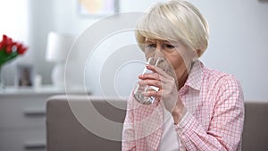 Upset senior woman feeling pain drinking water, health problems treatment