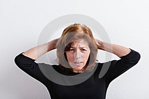 Upset senior woman holding head, studio shot against white wall.