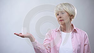 Upset senior woman holding pills bottle, unreliable pharmacological production