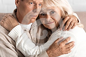 upset senior woman hugging with sick husband at home.