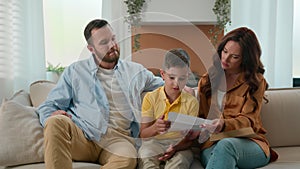 Upset shocked Caucasian family reading bad news on couch at home disappointed father mother son receiving paper letter
