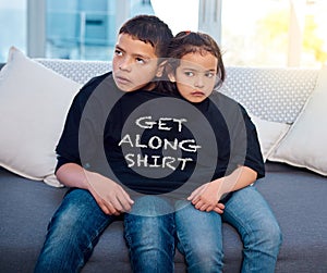 Upset, siblings and children on sofa in home with funny, comic and silly tshirt for joke. Fight, angry and young boy and