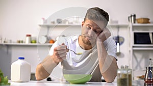 Upset single man eating tasteless cereals for breakfast, lack of appetite