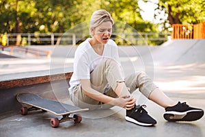 Upset skater girl holding her painful leg with skateboard near while spending time at skatepark