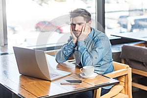 Upset stressed man freelancer working on laptop, looking at display, expressing sadness and sorrow.