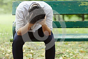 Upset stressed young Asian business man sitting on bench and suffering from severe depression. Unemployment and layoff concept