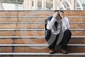 Upset stressed young Asian business man in suit with hands on head sitting on stairs. Unemployment and layoff concept