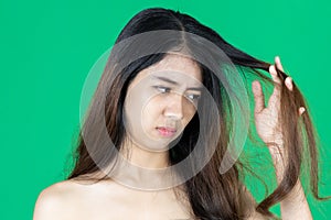 Upset stressed young Asian woman holding damaged dry hair on hands over green isolated background