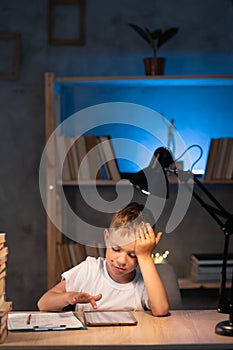 upset student boy with tablet pc computer and notebook learning online at home at night, schoolboy doing homework and