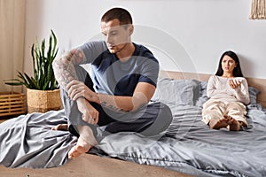 upset tattooed man sitting on bed