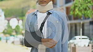 Upset teen boy wearing foam cervical collar and broken hand bandage, accident