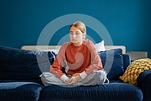 Upset teen girl sitting on sofa at home feeling lonely and frustrated