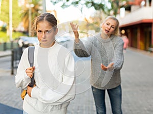 Upset teen girl walking on city street with worried mother reproaching her