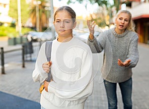Upset teen girl walking on city street with worried mother reproaching her