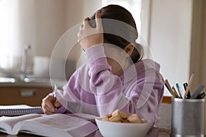 Upset teenage schoolgirl studying with textbook at home