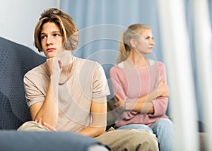 Upset teenager sitting on sofa after quarrel with mother