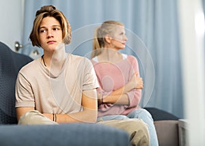 Upset teenager sitting on sofa after quarrel with mother