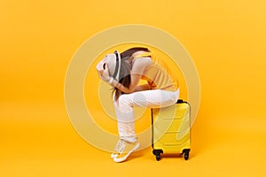 Upset tourist woman in summer casual clothes sit on suitcase put hands on head isolated on yellow orange background