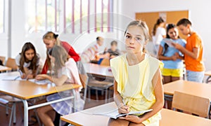 Upset tween girl sitting on table in schoolroom during recess