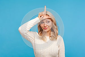 Upset unlucky woman with curly blond hair showing looser gesture holding finger near forehead, depressed with her fail